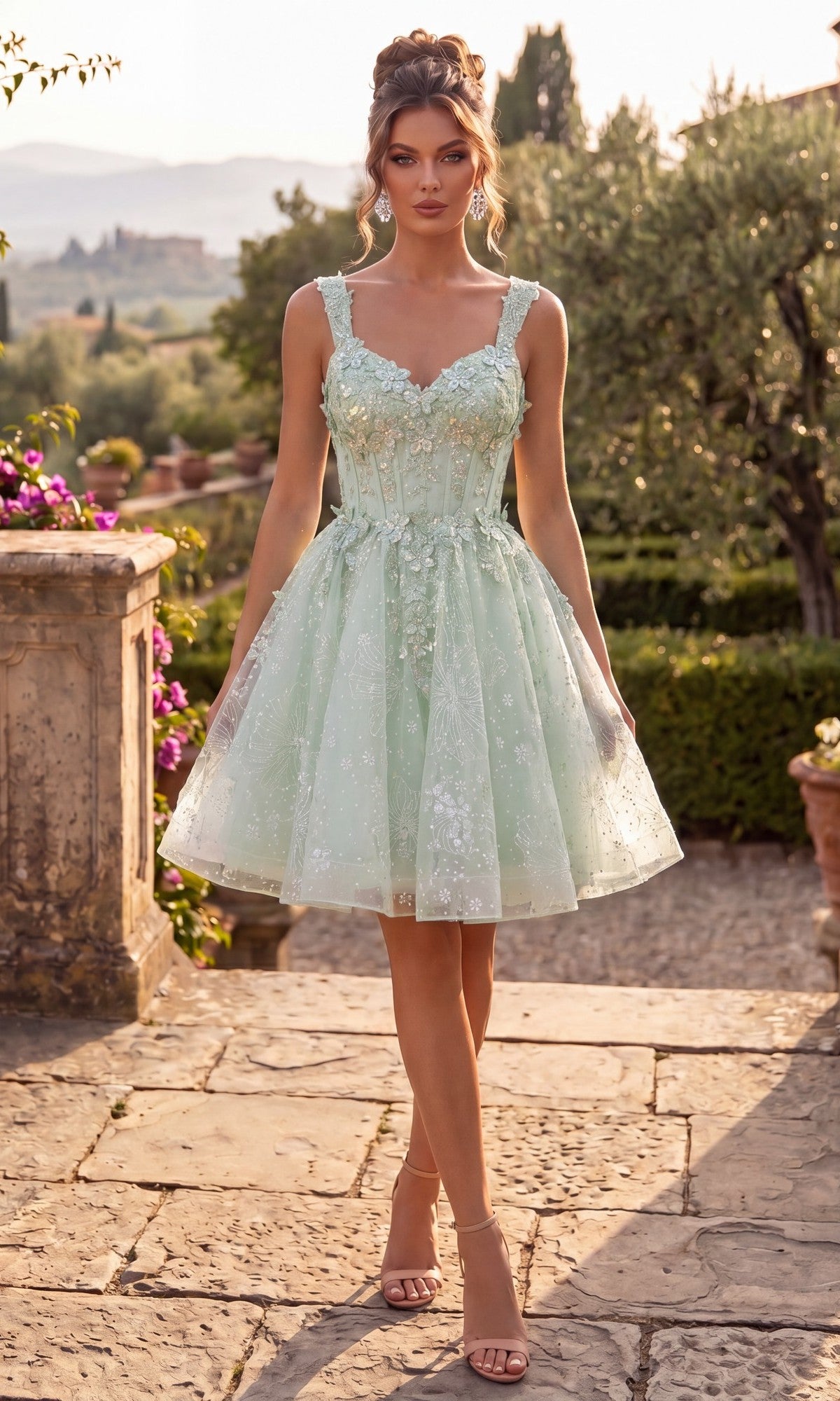 A woman wearing the Chicas C372 Short Homecoming Dress in sage—a light green, knee-length lace dress with a flattering fit-and-flare silhouette—paired with heels, stands on a stone path in a garden surrounded by greenery and flowers.